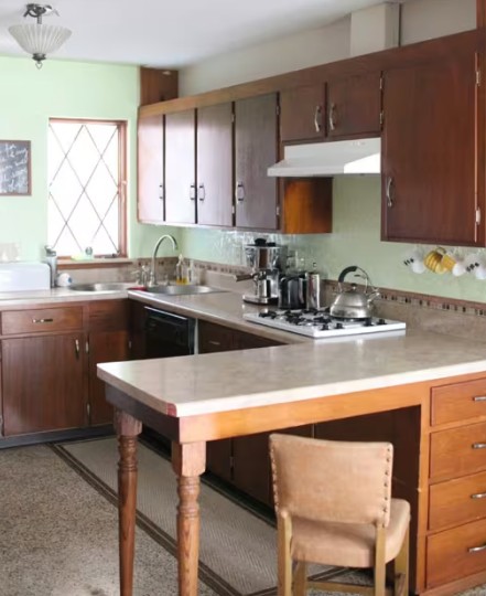 Dated kitchen with dark wood cabinets and pale green walls before repainting